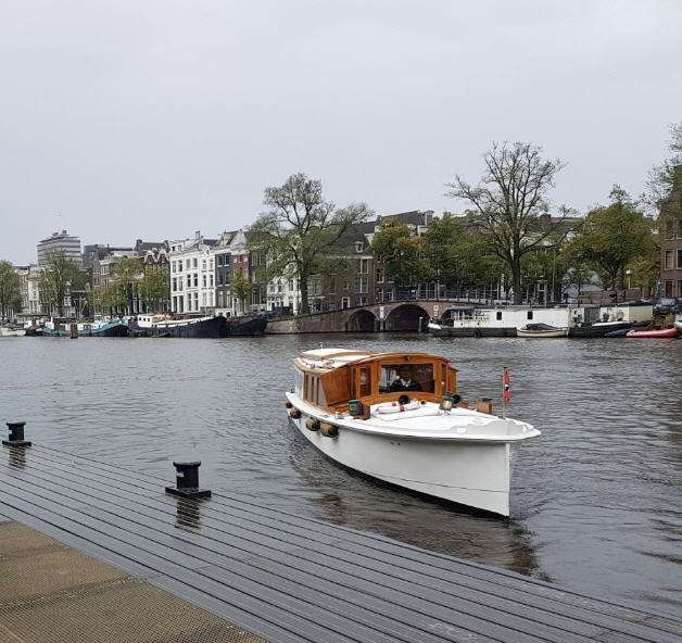 A classic salon boat with Amsterdam canal houses behind it